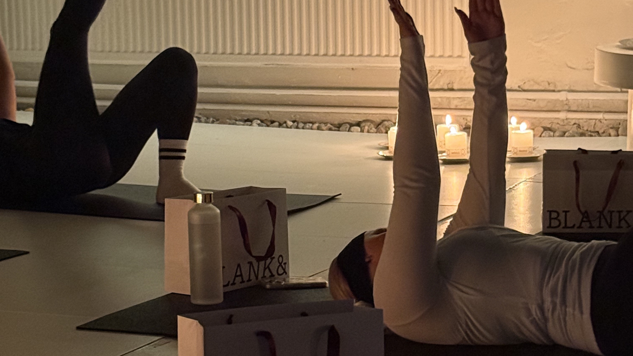 People practicing yoga in a dimly lit room with candles and branded boxes.